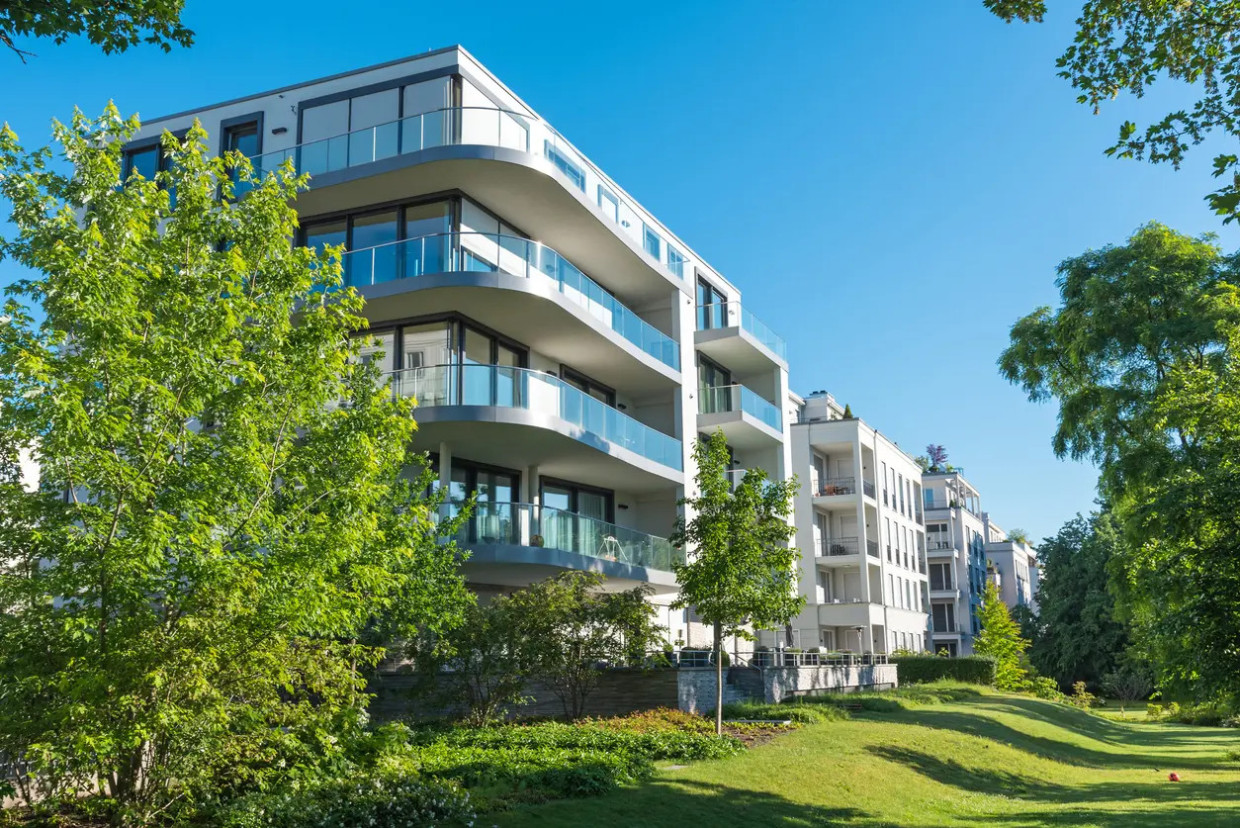 Immeuble résidentiel contemporain aux façades claires, entouré d'arbres et de pelouses.